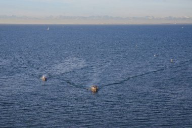 Adriyatik mavi denizi boyunca uzanan çok sayıda teknenin arka planında karla kaplı Alp dağları var..