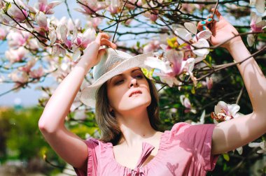 Bahar bahçesinde çiçek açan manolyalarla genç ve çekici bir kadının portresi. Bahar arka planı. Kadın Günü. Tebrik kartı. 