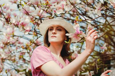 Bahar bahçesinde çiçek açan manolyalarla genç ve çekici bir kadının portresi. Bahar arka planı. Kadın Günü. Tebrik kartı. 