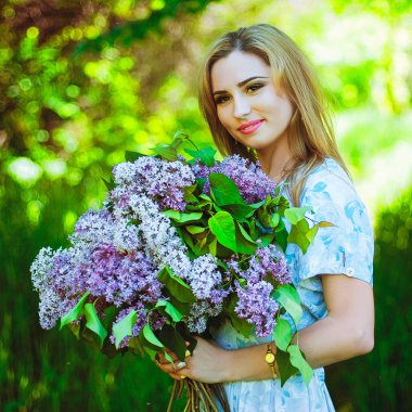Bahar bahçesinde bir buket leylakla genç ve çekici bir kadının portresi. Bahar arka planı. Kadın Günü. Tebrik kartı. 