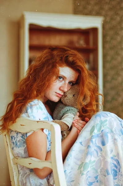 Portrait of cute redhead woman  with freckles in blue dress sitting with teddy bear toy at home. Natural beauty. Woman\'s Day. Greeting card.