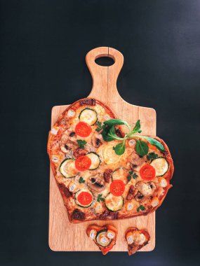 Lezzetli vejetaryen kalbi siyah zemin üzerinde Sevgililer Günü için domatesli, sebzeli ve peynirli pizza şeklinde. Romantik aşkın yaratıcı yemek konsepti. Üst manzara, düz uzanma.