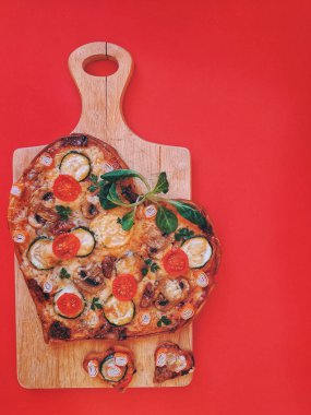 Lezzetli vejetaryen kalp şeklinde pizza, domates, sebze ve peynir, Sevgililer Günü için kırmızı arka planda tahta bir tahtada. Romantik aşkın yaratıcı yemek konsepti. Üst manzara, düz uzanma.