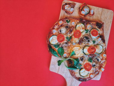 Lezzetli vejetaryen kalp şeklinde pizza, domates, sebze ve peynir, Sevgililer Günü için kırmızı arka planda tahta bir tahtada. Romantik aşkın yaratıcı yemek konsepti. Üst manzara, düz uzanma.