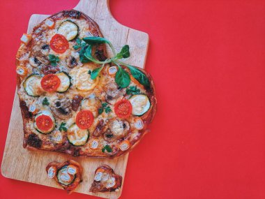 Lezzetli vejetaryen kalp şeklinde pizza, domates, sebze ve peynir, Sevgililer Günü için kırmızı arka planda tahta bir tahtada. Romantik aşkın yaratıcı yemek konsepti. Üst manzara, düz uzanma.