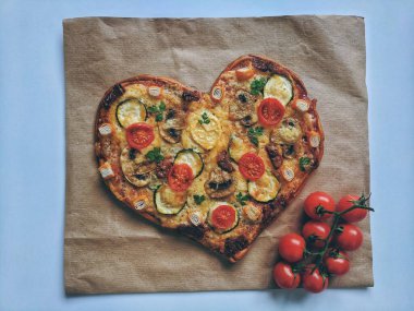 Kırmızı zemin üzerinde Sevgililer Günü için domatesli, sebzeli ve peynirli leziz vejetaryen kalp şeklinde pizza. Romantik aşkın yaratıcı yemek konsepti. Üst manzara, düz uzanma.