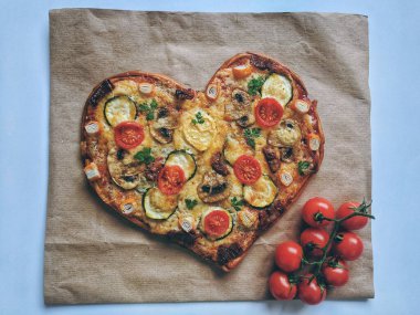 Kırmızı zemin üzerinde Sevgililer Günü için domatesli, sebzeli ve peynirli leziz vejetaryen kalp şeklinde pizza. Romantik aşkın yaratıcı yemek konsepti. Üst manzara, düz uzanma.