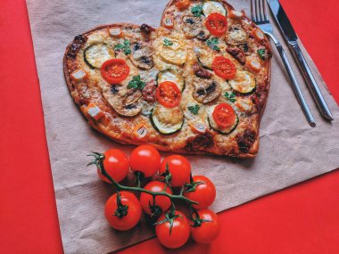 Kırmızı zemin üzerinde Sevgililer Günü için domatesli, sebzeli ve peynirli leziz vejetaryen kalp şeklinde pizza. Romantik aşkın yaratıcı yemek konsepti. Üst manzara, düz uzanma.