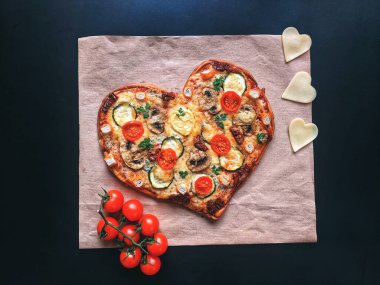 Lezzetli vejetaryen kalbi siyah zemin üzerinde Sevgililer Günü için domatesli, sebzeli ve peynirli pizza şeklinde. Romantik aşkın yaratıcı yemek konsepti. Üst manzara, düz uzanma.