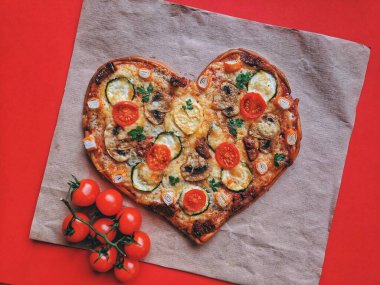 Kırmızı zemin üzerinde Sevgililer Günü için domatesli, sebzeli ve peynirli leziz vejetaryen kalp şeklinde pizza. Romantik aşkın yaratıcı yemek konsepti. Üst manzara, düz uzanma.