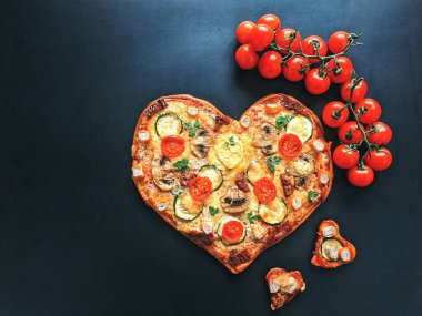 Lezzetli vejetaryen kalbi siyah zemin üzerinde Sevgililer Günü için domatesli, sebzeli ve peynirli pizza şeklinde. Romantik aşkın yaratıcı yemek konsepti. Üst manzara, düz uzanma.