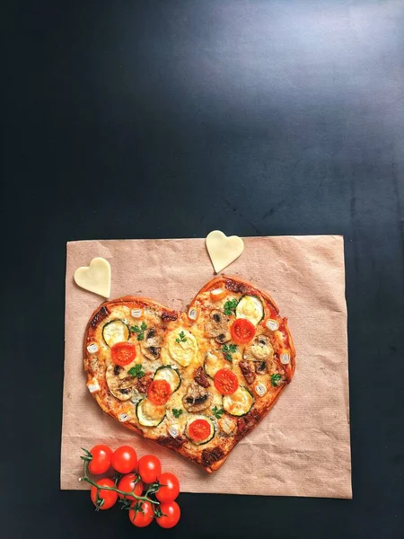 Delicious vegetarian heart shaped pizza with tomatoes, vegetables and cheese for Valentine\'s Day on black background. Creative food concept of romantic love. Top view, flat lay.