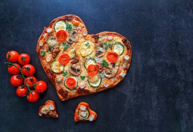 Lezzetli vejetaryen kalbi siyah zemin üzerinde Sevgililer Günü için domatesli, sebzeli ve peynirli pizza şeklinde. Romantik aşkın yaratıcı yemek konsepti. Üst manzara, düz uzanma.
