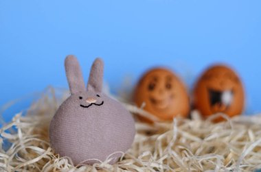 Corona virüsü (COVID19) korumalı yaratıcı Paskalya yumurtaları. Tıbbi maske takan ve mavi arka planda oyuncak tavşan takan karalama yüzlü tavuk yumurtaları. Düz konum, üst görünüm, maket, kopyalama alanı.