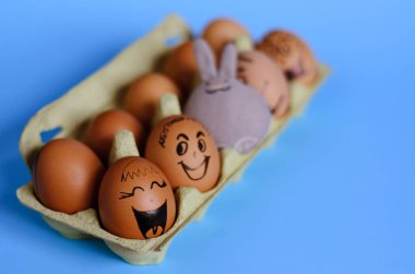 Corona virüsü (COVID19) korumalı yaratıcı Paskalya yumurtaları. Tıbbi maske takan ve mavi arka planda oyuncak tavşan takan karalama yüzlü tavuk yumurtaları. Düz konum, üst görünüm, maket, kopyalama alanı.