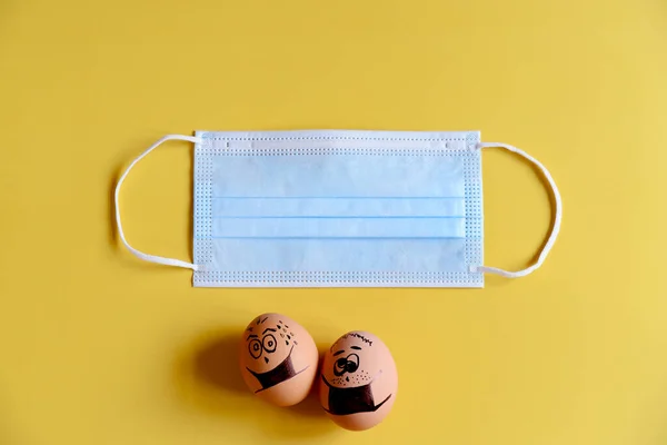 Creative Easter eggs with Corona virus (COVID19) protection concepts. Chicken eggs with doodle faces wearing medical masks with pills on yellow background. DIY. Flat lay, top view, copy space.