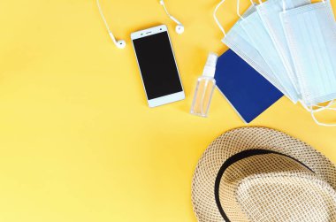 Covid-19 ve yeni normal kavramlardan sonra seyahat et. Tıbbi yüz maskesi, el jeli dezenfektan, kulaklık ve sarı arka planda plaj şapkası. Koronavirüsü önlemek için yaratıcı fikirler.