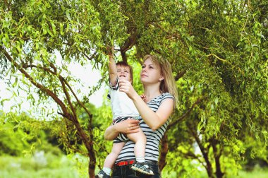 Mutlu aile kavramı. Anne ve oğlu güneşli bir günde parkta oynuyor ve bir yaz yürüyüşünde gülüyorlar. Aile tatili ve birliktelik, seçici odaklanma