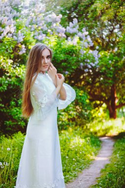 Bahar bahçesinde çiçekli uzun beyaz gelinlikli çekici bir kadının portresi. Bahar arka planı. Düğün konsepti. Tebrik kartı. 