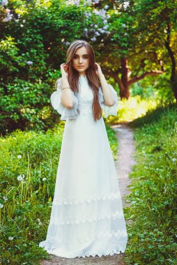 Bahar bahçesinde çiçekli uzun beyaz gelinlikli çekici bir kadının portresi. Bahar arka planı. Düğün konsepti. Tebrik kartı. 