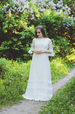 Bahar bahçesinde çiçekli uzun beyaz gelinlikli çekici bir kadının portresi. Bahar arka planı. Düğün konsepti. Tebrik kartı. 