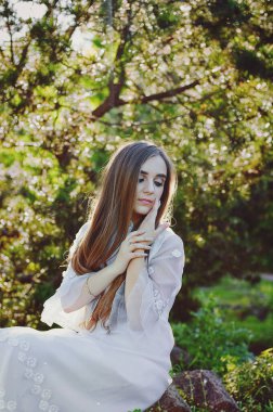 Bahar bahçesinde çiçekli uzun beyaz gelinlikli çekici bir kadının portresi. Bahar arka planı. Düğün konsepti. Tebrik kartı. 