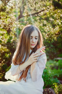 Bahar bahçesinde çiçekli uzun beyaz gelinlikli çekici bir kadının portresi. Bahar arka planı. Düğün konsepti. Tebrik kartı. 