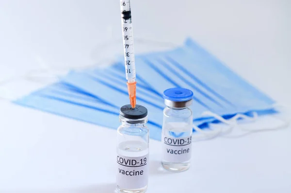 Creative ideas of vaccination concept. Top view of syringe with medical masks and vaccine vial glass bottles for vaccination against COVID-19. Coronavirus pandemic. Copy space.