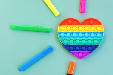 Renkli işaretlerin ve stres önleyici oyuncakların üst görüntüsü yeşil arka planda gökkuşağı kalbini yakın planda tutar. Çocuk oyuncaklarının yaratıcı ve komik kavramları. Popüler oyuncak. Moda Oyuncağı 2021.