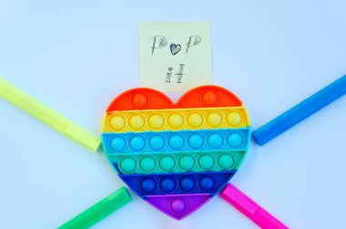 Renkli işaretlerin ve stres önleyici oyuncakların üst görüntüsü mavi arka planda gökkuşağı kalbini ortaya çıkarır. Çocuk oyuncaklarının yaratıcı ve komik kavramları. Popüler oyuncak. Moda Oyuncağı 2021.