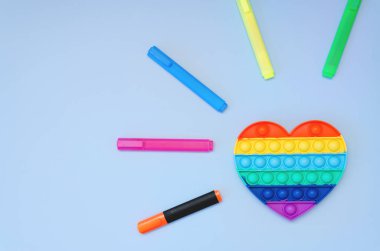Renkli işaretlerin ve stres önleyici oyuncakların üst görüntüsü mavi arka planda gökkuşağı kalbini ortaya çıkarır. Çocuk oyuncaklarının yaratıcı ve komik kavramları. Popüler oyuncak. Moda Oyuncağı 2021.