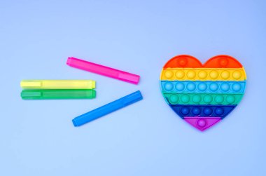 Renkli işaretlerin ve stres önleyici oyuncakların üst görüntüsü mavi arka planda gökkuşağı kalbini ortaya çıkarır. Çocuk oyuncaklarının yaratıcı ve komik kavramları. Popüler oyuncak. Moda Oyuncağı 2021.