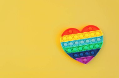 Renkli işaretlerin ve stres önleyici oyuncakların üst görüntüsü sarı arka planda gökkuşağı kalbini yakın plana koyar. Çocuk oyuncaklarının yaratıcı ve komik kavramları. Popüler oyuncak. Moda Oyuncağı 2021.