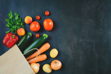 Alışveriş ya da sağlıklı yiyecek teslimatı. Yiyecek süpermarketi ve temiz vegan yeme konsepti. Taze sebzeler ve meyveler: Havuç, patates, kabak, siyah arka planda domates. Boşluğu kopyala.