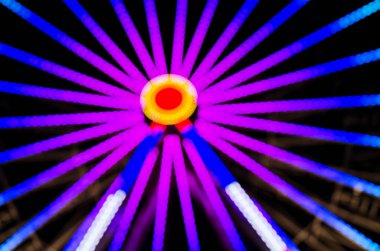 Gece Lunaparkın bulanık ve bulanık görüntüsü. Gece gökyüzüne karşı Bokeh ışıkları içinde dönme dolap ve lunapark treni. Eğlence parkı gezisi. Soyut arkaplan ve dokular.