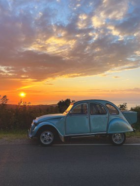 Güzel mavi retro araba Citroen, yaz mevsiminde Slovenya 'da Adriyatik Denizi' nde gün batımına karşı yolda duruyor. Yeşil tepelere ve zeytin ağaçlarına bakın. 