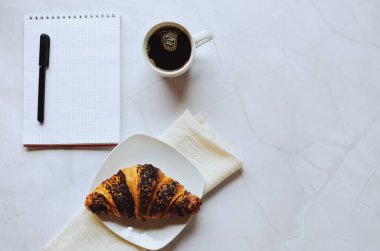 Sabah iş adamı elinde defter, kalem, bir fincan sıcak kahve ve beyaz arka planda kruvasanla çalışıyor. Üst görünüm, kopyalama alanı, modelleme. Düz yatıyordu. Sağlıklı gıda konsepti.