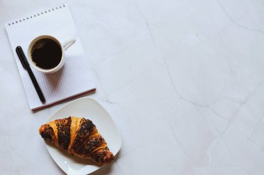 Sabah iş adamı elinde defter, kalem, bir fincan sıcak kahve ve beyaz arka planda kruvasanla çalışıyor. Üst görünüm, kopyalama alanı, modelleme. Düz yatıyordu. Sağlıklı gıda konsepti.