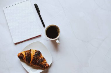 Sabah iş adamı elinde defter, kalem, bir fincan sıcak kahve ve beyaz arka planda kruvasanla çalışıyor. Üst görünüm, kopyalama alanı, modelleme. Düz yatıyordu. Sağlıklı gıda konsepti.