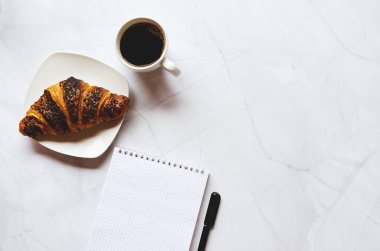 Sabah iş adamı elinde defter, kalem, bir fincan sıcak kahve ve beyaz arka planda kruvasanla çalışıyor. Üst görünüm, kopyalama alanı, modelleme. Düz yatıyordu. Sağlıklı gıda konsepti.