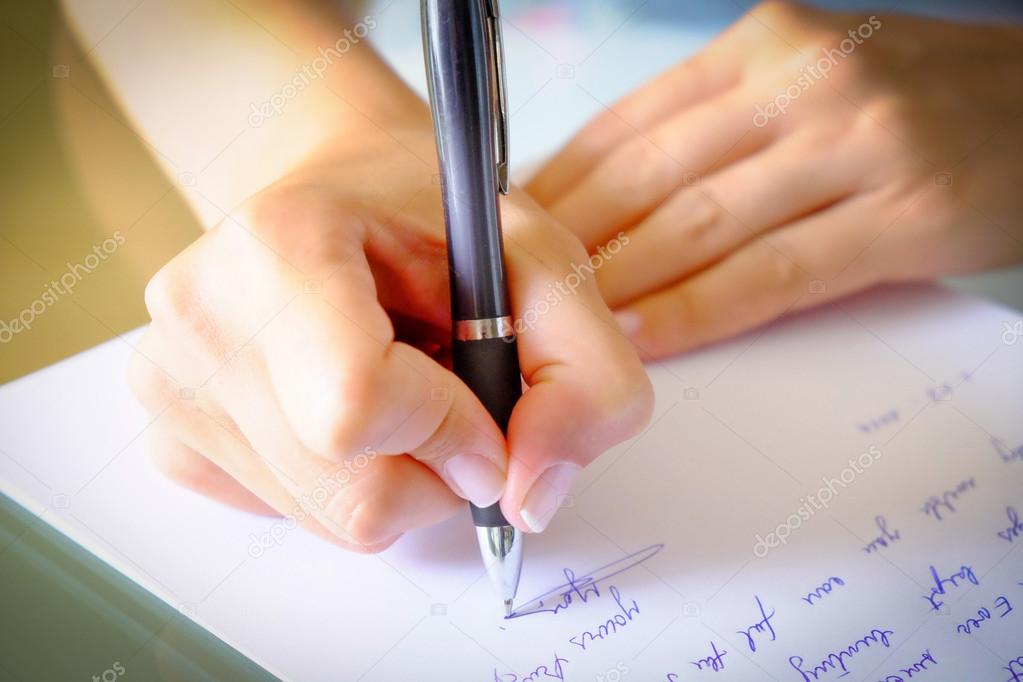 Girl Writing down a letter on a white sheet of paper with a black pen.