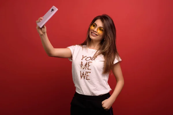 Çekici ve mutlu bir kadının portresi kırmızı arka planda izole edilmiş selfie yapıyor.