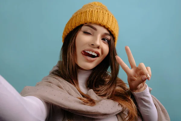 Komik, neşeli, genç bir kadın selfie çekiyor. Atkı takan ve sarı şapkalı gülümseyen kız.