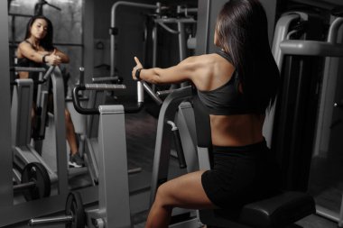 Aynanın önünde egzersiz makinesinde egzersiz yapan güçlü, kaslı, sportif kadının arka planı.