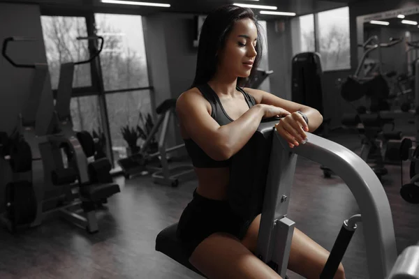 Feliz mujer deportiva atractiva sonríe y mirando su pulsera deportiva —  Fotos de Stock