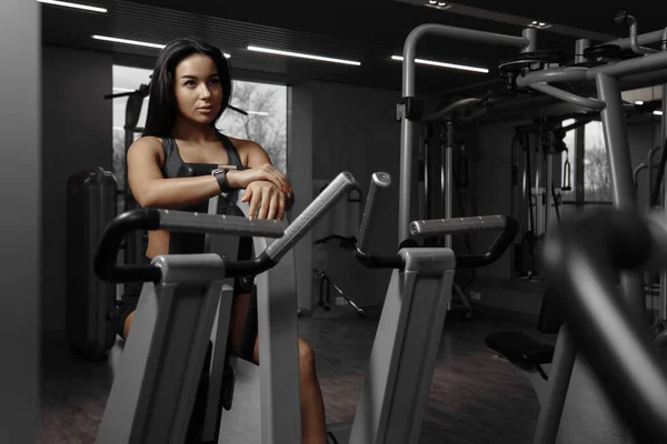 Vit kvinna sitter på gymmet maskin och tittar på sig själv i spegeln, vilar efter träning. — Stockfoto