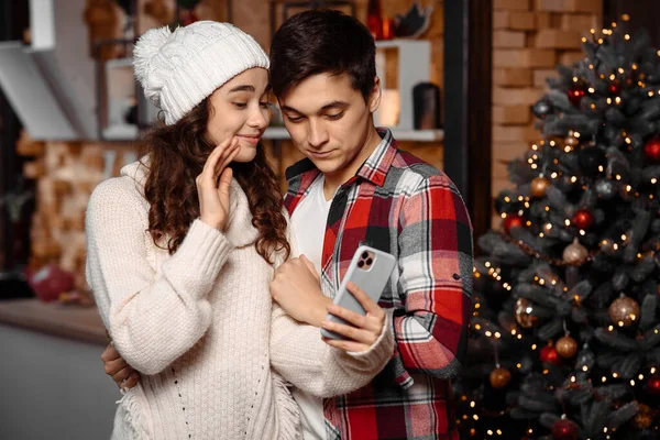 Ευτυχισμένο νεαρό ζευγάρι που ελέγχει τα Χριστούγεννα μηνύματα σε ένα smartphone Φωτογραφία Αρχείου