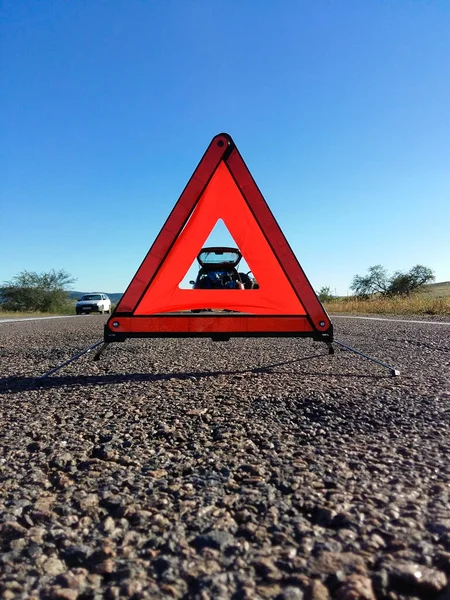 Warning Triangle for Breakdown Roadside Emergency standing on asphalt road against broken car with open trunk. Rural landscape with clear blue sky
