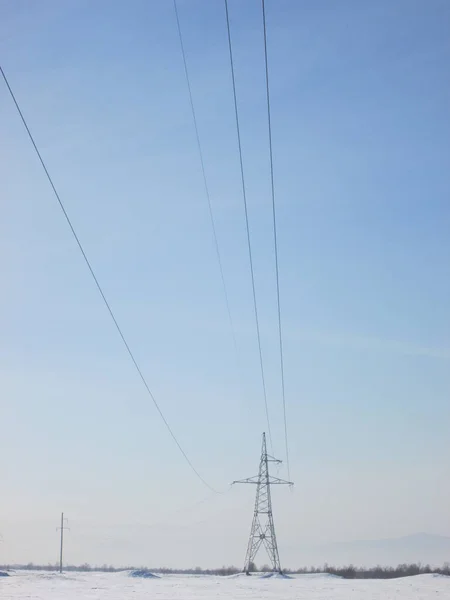 Power line, electric metal pole with wires in the winter steppe covered with snow