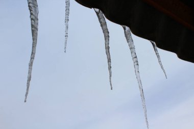 Baharda çatıdan sarkan Mavi Bulutlu Gökyüzüne karşı kristal buz saçakları